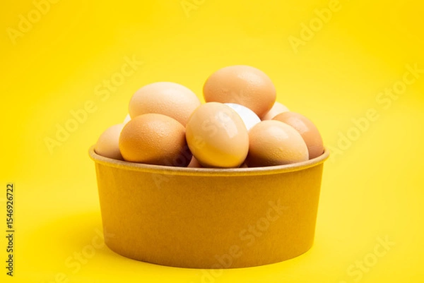 Obraz Brown eggs in paper bowl – front view, on yellow background