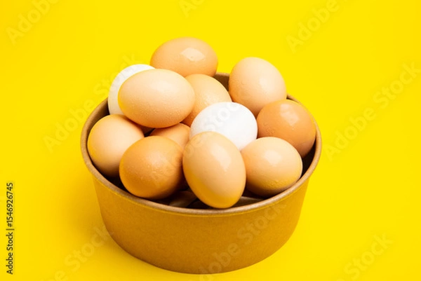 Obraz Brown and white eggs in paper bowl – top view, yellow background