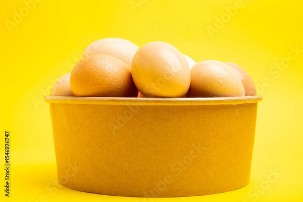 Obraz Brown eggs in paper bowl – front view,yellow background
