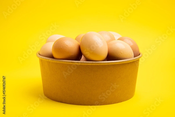 Obraz Brown eggs in paper bowl on yellow background