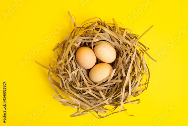 Obraz Three eggs in straw nest – top view,yellow background