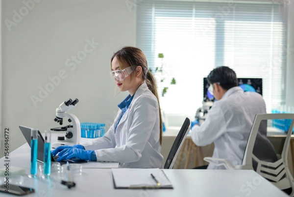 Fototapeta Scientist working with laptop in laboratory with microscope and test tubes