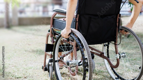 Fototapeta cropped shot, middle age female on wheelchair and hand grip on wheel on grass field at home she resting after being sick