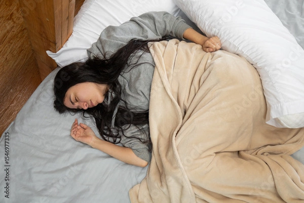 Fototapeta Close-up from above of a young woman peacefully sleeping, wrapped from the waist down in soft sheets inside a cozy glamping tent. An intimate and calm resting moment.

