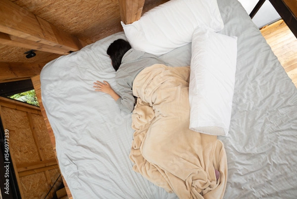 Fototapeta A young woman sleeps peacefully, wrapped in soft white sheets from the waist down, seen from above in a cozy glamping tent. A serene, intimate moment of rest.

