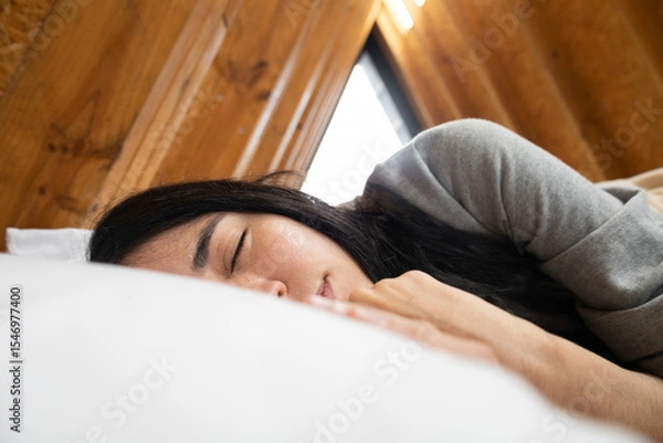 Fototapeta A young woman sleeps peacefully under a warm blanket in a rustic glamping tent, surrounded by soft light and natural textures. A quiet, intimate moment of deep rest.

