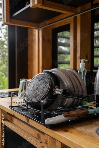 Fototapeta Plates neatly drying on a dish rack inside a warm, rustic kitchen, showcasing simple, homey living with natural wood elements and soft, inviting light.

