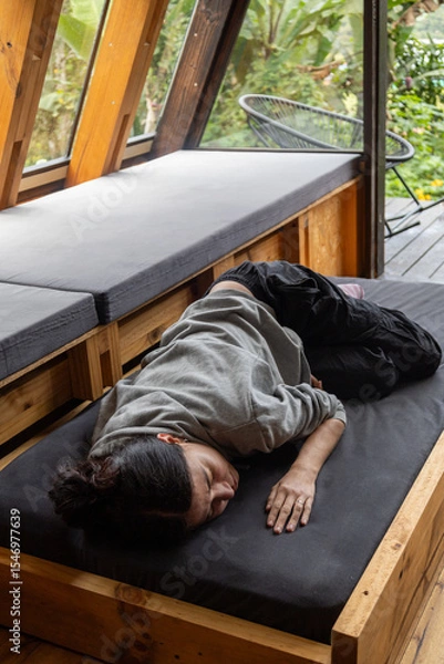 Fototapeta A young woman rests comfortably lying on a wooden bed frame that is pulled out from a drawer inside a stylish glamping tent. The scene blends rustic charm with modern outdoor luxury, capturing a peace