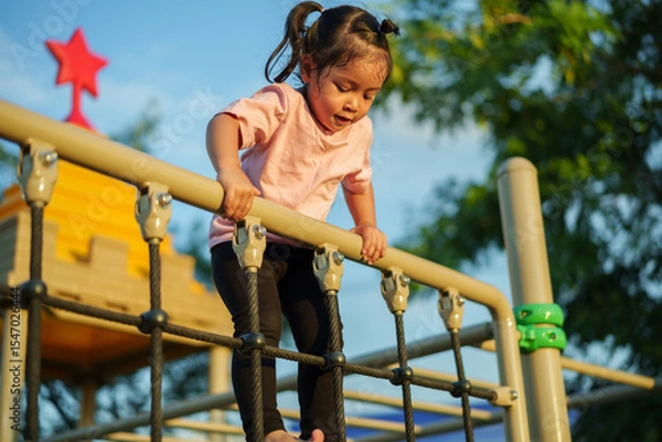 Fototapeta happy toddler girl playing with climbing ropes net at a outdoor playground in park
