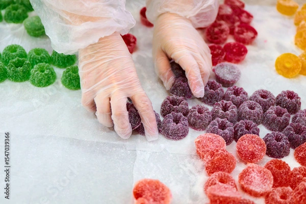 Fototapeta Hands sorting colorful marmalade candies on a white surface in a candy production area