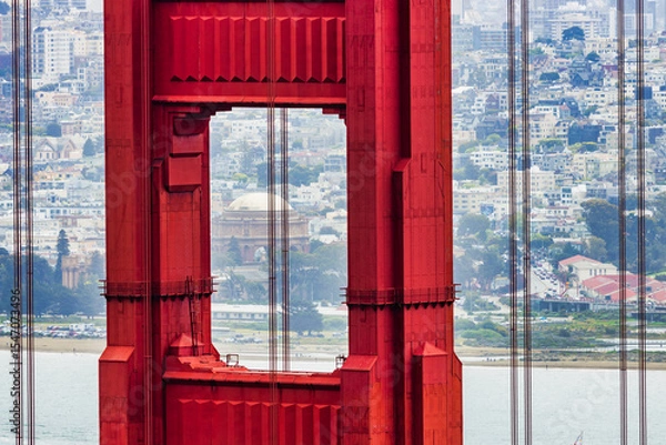 Fototapeta Close-up of Golden Gate Bridge tower with Palace of Fine Arts in the background, San Francisco cityscape and boats on the bay visible through the iconic red structure.