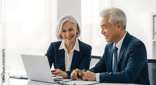 Obraz Collaboration and Professionalism: Two mature business people share a moment of focus and collaboration over a laptop.