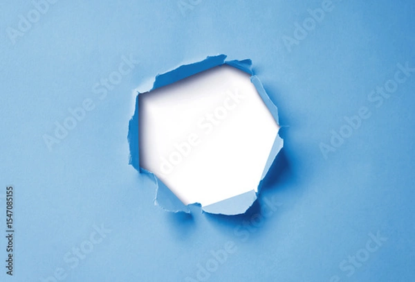 Fototapeta Close-up image of a blue paper sheet with a jagged hole torn through the center, revealing a transparent background.