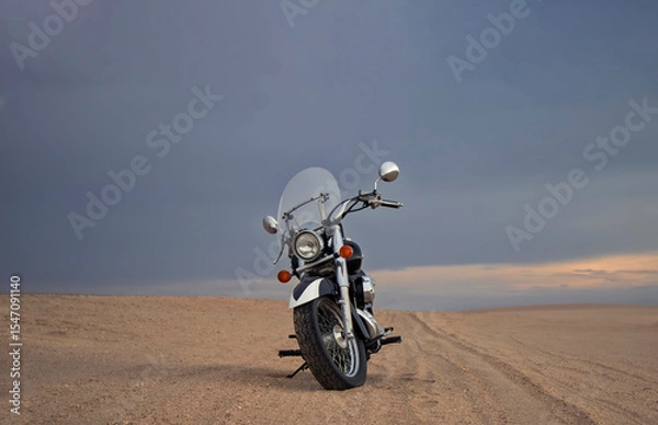 Fototapeta Off-road motorcycle standing still in the open desert beneath heavy clouds. A strong visual of freedom, rugged adventure, and the thrill of riding through wild, untamed terrain.
