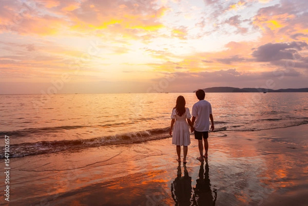 Obraz Young happiness Asian couple traveler relaxing and watching beautiful Sunset on the tranquil beach, Traveling on summer vacation concept