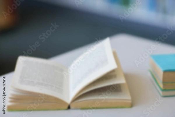 Obraz Flat design open paperback book is resting on tabletop with colorful book stack, blurred bookshelf