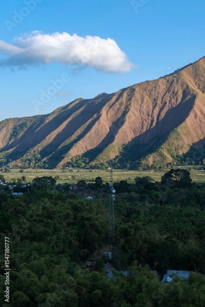Fototapeta Majestic view of Pergasingan Hill glowing under soft morning light, seen from Selong Hill in Sembalun, Lombok—where dramatic ridgelines meet tranquil rural charm.