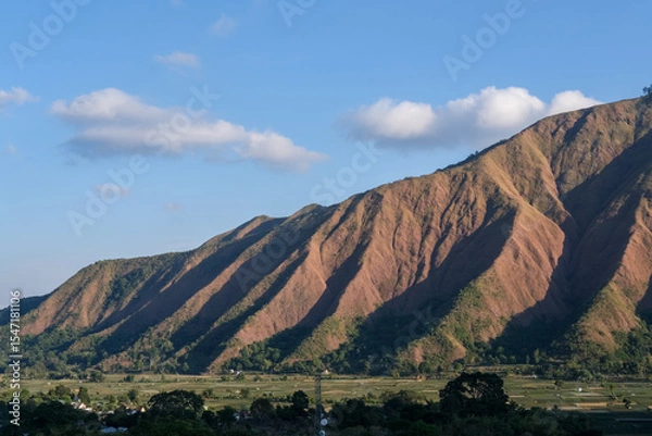Fototapeta Majestic view of Pergasingan Hill glowing under soft morning light, seen from Selong Hill in Sembalun, Lombok—where dramatic ridgelines meet tranquil rural charm.