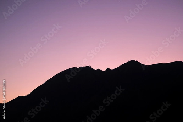 Fototapeta Glowing twilight sky blankets the rolling hills of Sembalun, Lombok, painting the horizon in soft purples and oranges as mountain silhouettes fade into serene dusk.