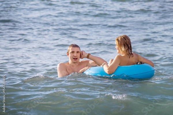 Fototapeta A young couple swims in the sea with an inflatable circle