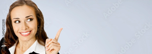 Fototapeta Banner wide image - happy smile businesswoman showing pointing advertise. Business woman executive employee bank manager, isolated against grey gray wall background with free ad text space
