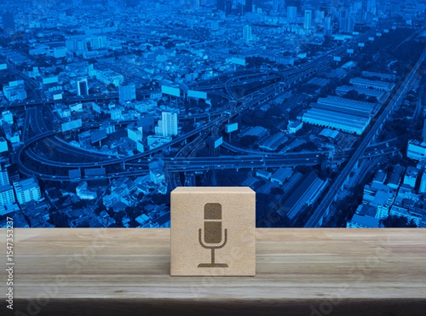 Fototapeta Microphone flat icon on wood block cube on wooden table over modern city tower, street, expressway and skyscraper, Technology communication concept