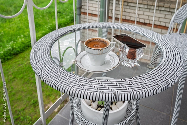 Fototapeta A cup of coffee, a smartphone on a glass table on a balcony.	