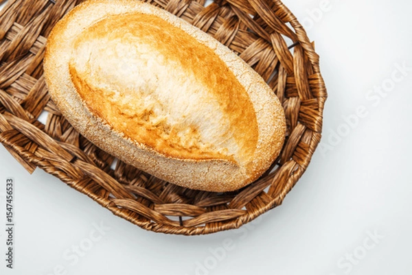 Obraz Freshly baked bread in a woven basket on a light background