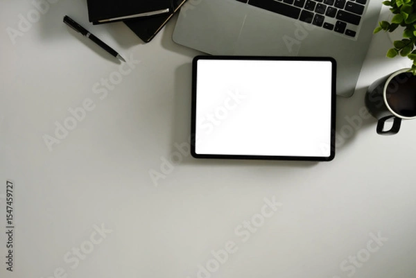 Fototapeta Top view of digital tablet with blank screen, laptop, notebook, and coffee cup on a white desk