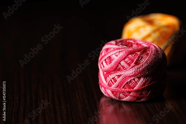 Fototapeta Skeins of colored melange threads of pink and yellow lie on a dark wooden table. Selective focus. Copyspace.