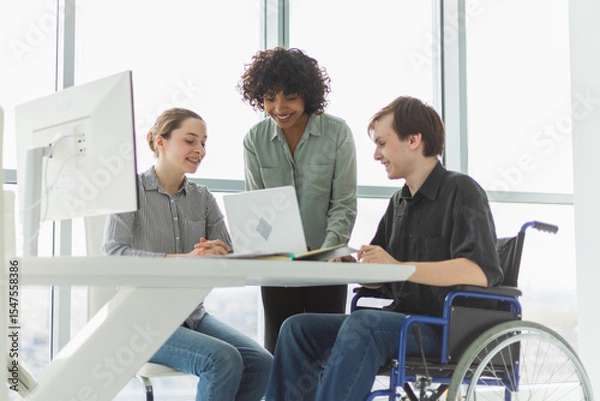 Fototapeta Teamwork brainstorm. Diverse multiracial colleagues man in chair for people with disability working together. Group of people sitting in creative office discussing business. Young professional team