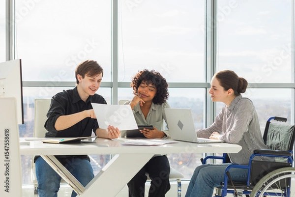 Fototapeta Teamwork brainstorm. Diverse multiracial colleagues woman in chair for people with disability working together. Group of people sitting in creative office discussing business. Young professional team
