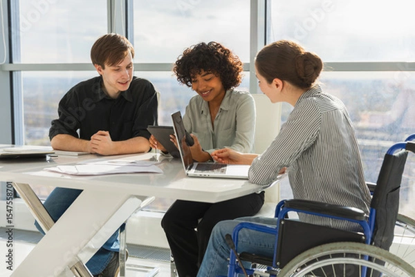 Fototapeta Teamwork brainstorm. Diverse multiracial colleagues woman in chair for people with disability working together. Group of people sitting in creative office discussing business. Young professional team