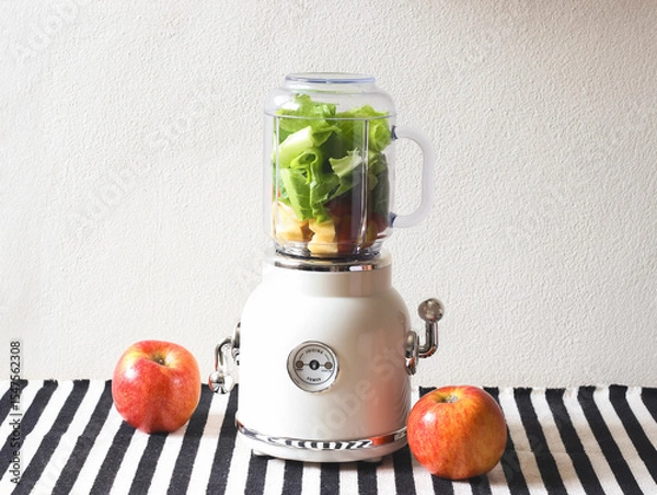 Fototapeta Front view of  white vintage blender or smoothie maker machine  with an apple on  black and white stripe table cloth and white wall. Healthy drink making.