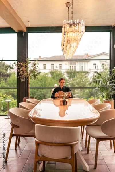 Obraz Restaurant menu chandelier: Woman reads menu in luxury restaurant in daylight, choosing meals.
