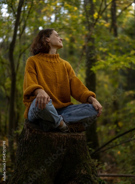 Fototapeta Young Caucasian woman enjoying autumn nature and weather sitting on a tree stump in autumn forest