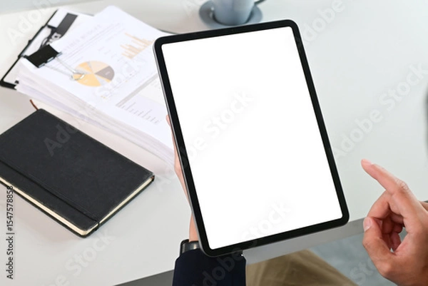 Obraz A person is holding a tablet with a white screen and a black book on the table. The tablet is pointing to a tablet