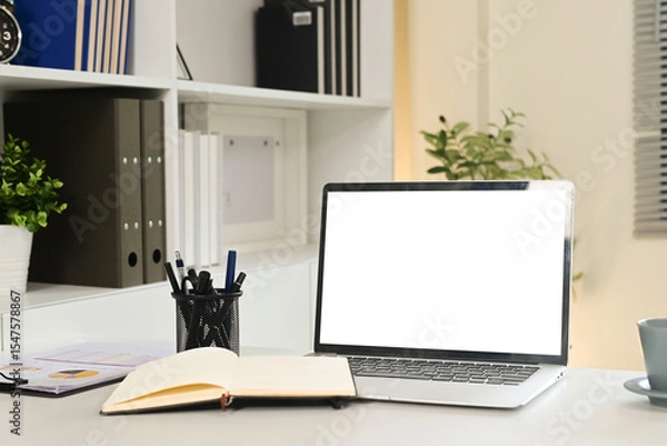 Obraz A laptop sits on a desk with a notebook and a cup of coffee. The laptop is open to a blank screen