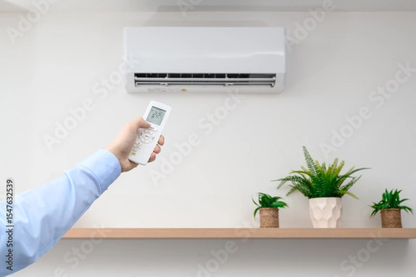 Fototapeta Turn on the air conditioning at home with the remote control, the device hangs on the wall