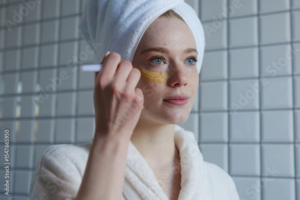 Fototapeta A Woman is Applying a Face Mask in a Relaxing SpaLike Setting, Embracing Beauty and Care