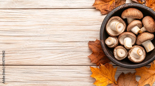 Fototapeta Shiitake mushrooms in wooden bowl surrounded by autumn leaves on rustic wooden background.