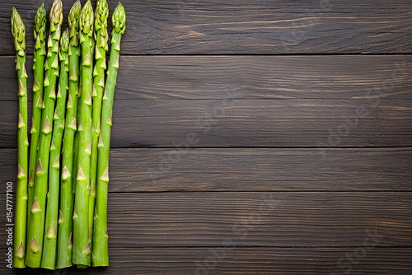 Fototapeta Fresh green asparagus spears are arranged neatly on a dark rustic wooden surface background.
