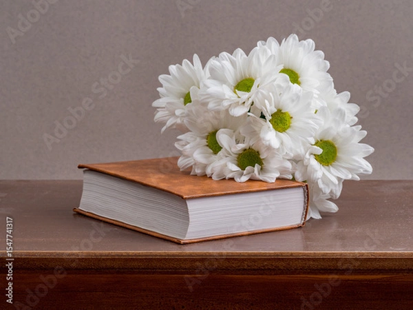 Fototapeta a bouquet of chamomile flowers and old books on a table on a natural background. a composition with books in a rustic style. the concept of reading and relaxing. the summer season. template for regist