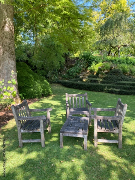 Obraz Old wooden garden furniture set placed in a lush garden, evoking rustic charm and outdoor relaxation in a natural setting.