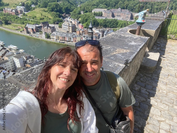 Obraz Happy couple taking a selfie on the balcony of Dinant citadel, with panoramic view of the city and Meuse River in the background.