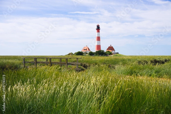 Obraz Idyllischer Leuchtturm Westerhever umgeben von grünem Grass unter blauem Himmel
