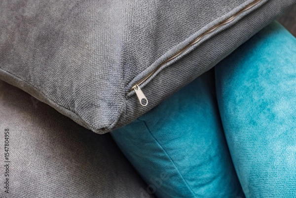 Fototapeta Close-up cushions with zipper detail. A close-up view of stacked cushions featuring a mix of gray and turquoise fabrics. Use for home decor, interior design, and textile themes.
