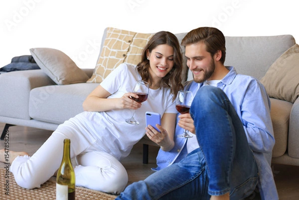 Fototapeta Happy couple sitting, relaxing on floor in living room, drinking red wine. Smiling young husband and wife rest at home enjoy romantic date on family weekend together on a transparent background