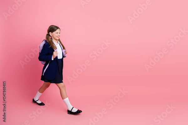 Obraz Charming schoolgirl in uniform walking confidently carrying a backpack against a stylish pink background