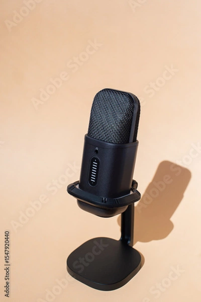 Fototapeta Black studio microphone on stand with beige background in natural light